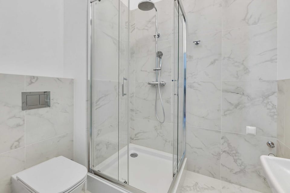 A stylish bathroom with marble-patterned tiles, a glass walk-in shower, and sleek white fixtures.
