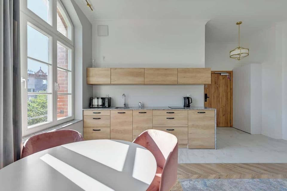 Contemporary charm with its sleek, minimalist wooden cabinetry, elegant countertops, and soft, natural light streaming through large windows, offering a harmonious and airy atmosphere.