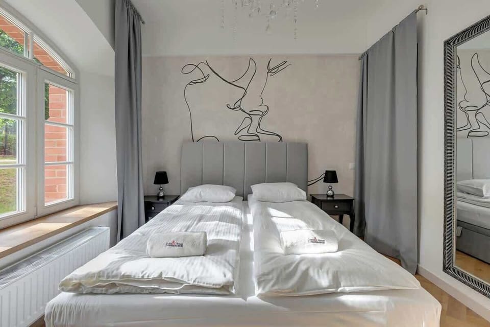 Elegantly adorned with minimalist décor, a striking abstract line drawing on the wall, luxurious grey curtains, and a statement mirror, all complemented by the sleek bed