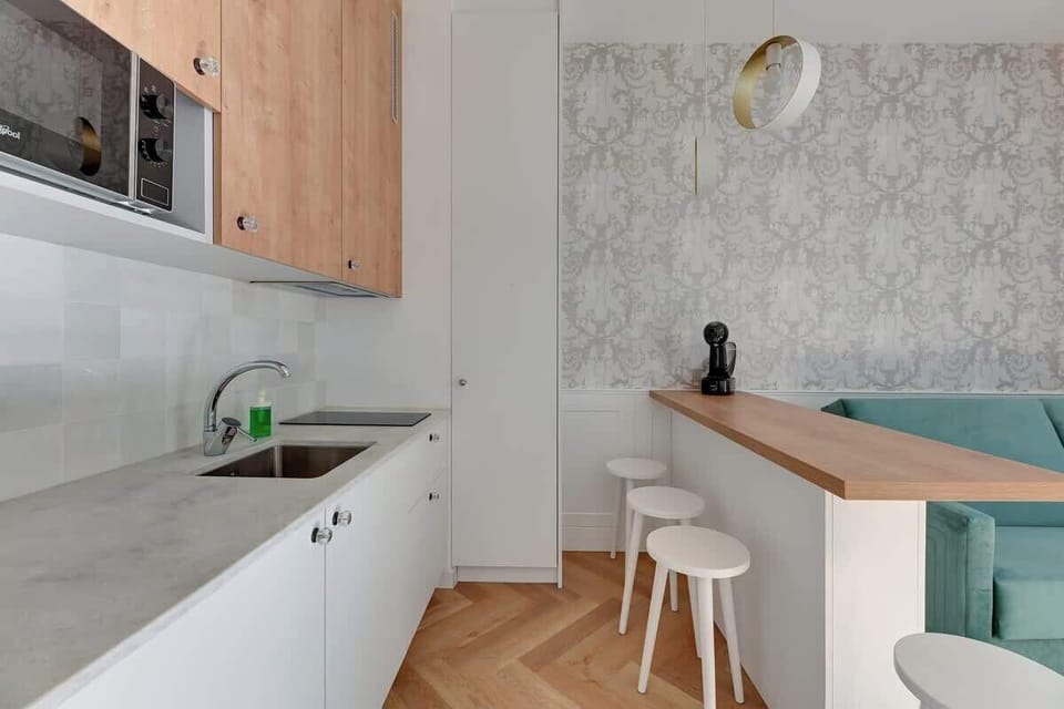 Warm wooden countertop, minimalist stools, and striking light fixtures, blending contemporary design with functional simplicity in a bright and airy space.