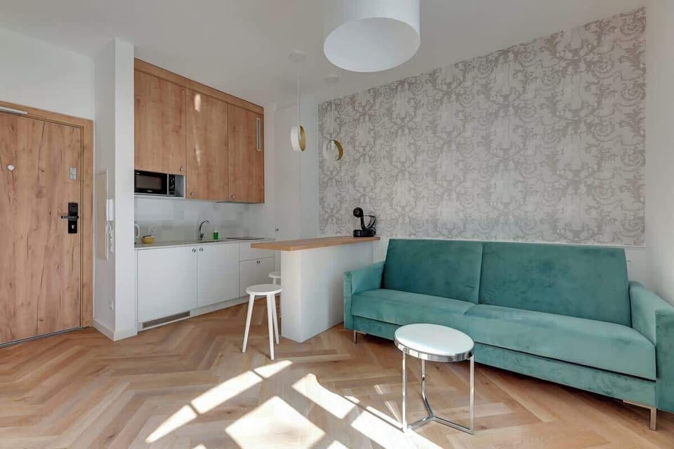 Soft pastel hues with elegant modern elements, featuring a plush green velvet sofa, sleek chrome accents, and a spacious, minimalist kitchen with wood finishes, all bathed in abundant natural light.