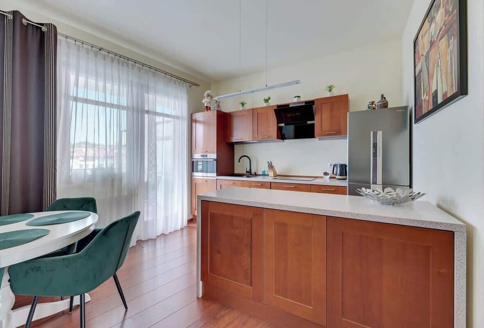 A modern kitchen with wooden cabinets, an oven, and a dining area with a round glass table and chairs.