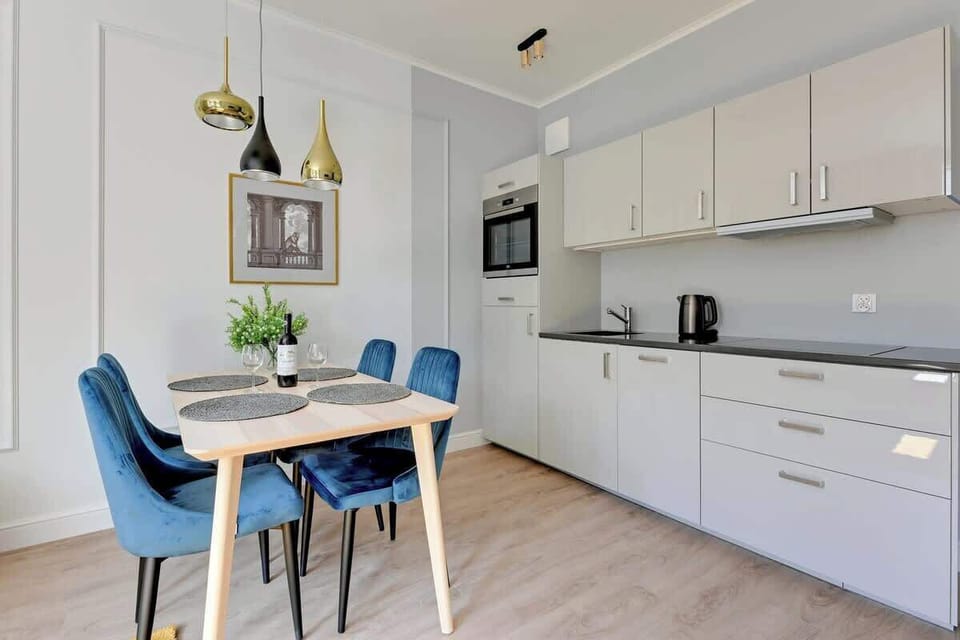 A spacious dining area with a large table, chairs, and decorative lighting, next to an open kitchen.