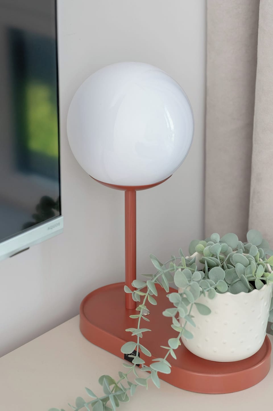 A small, well-decorated corner with a round lamp and a plant in a terracotta pot sits on a windowsill, adding a touch of homey decor.