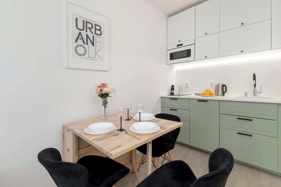 A modern kitchenette with light green cabinets, equipped with appliances such as a microwave, kettle, and stovetop, offers a sleek, minimalist design.