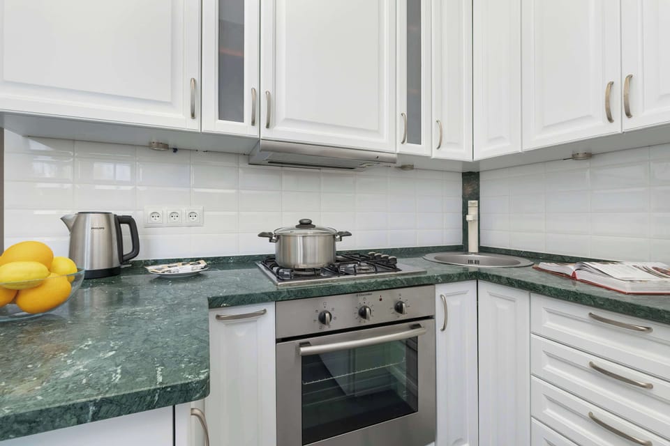 A kitchen featuring green stone countertops, white cabinets, and modern appliances, including a stovetop and kettle.
