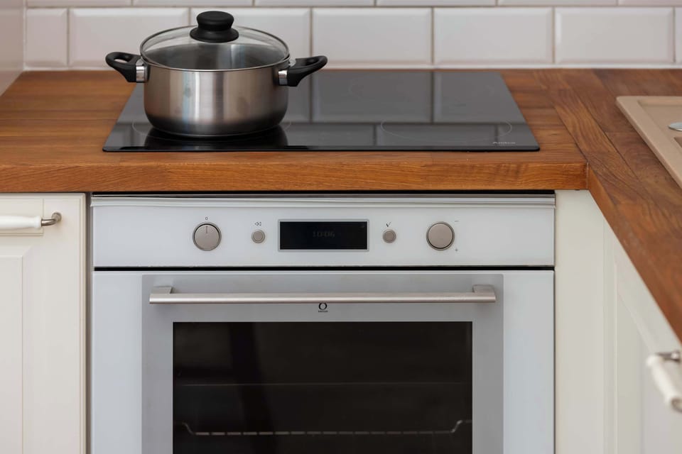 A close-up view of a white oven with a steel pot resting on the wooden counter above it.


