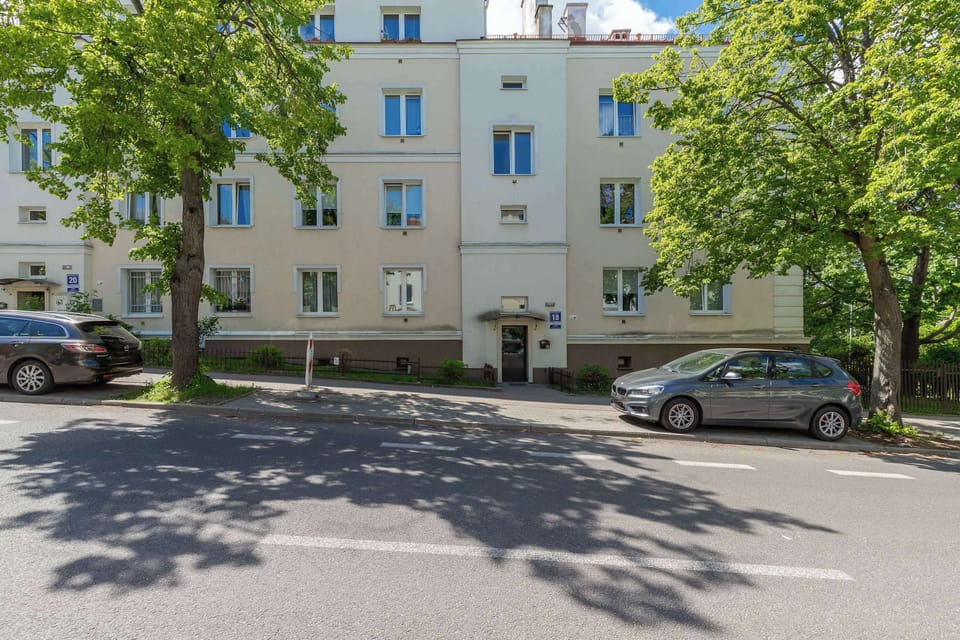 A wide-angle view of a peaceful street with mature trees and low-rise apartment blocks.

