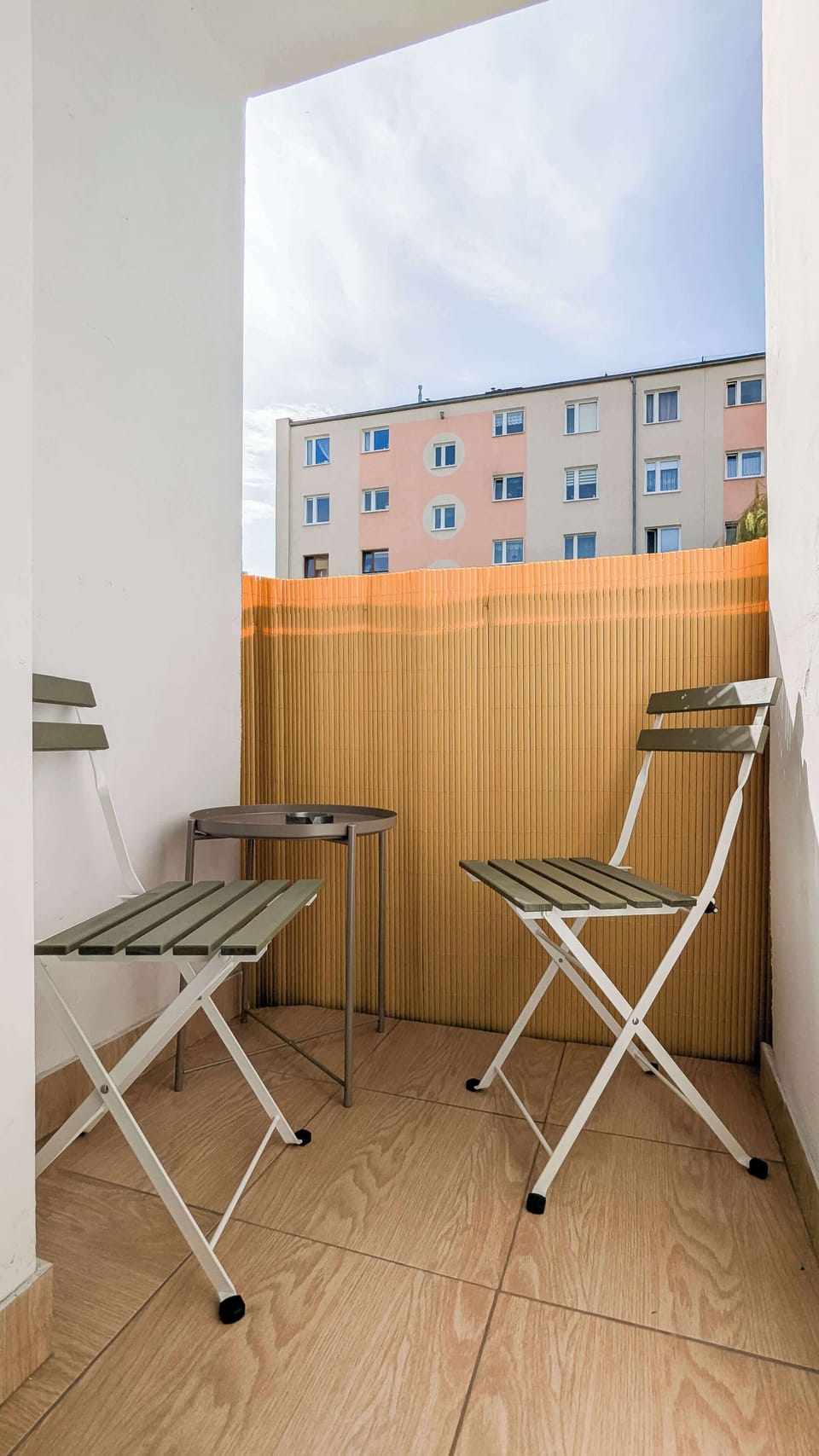 A small balcony furnished with a folding table and two chairs, perfect for enjoying fresh air and morning coffee.