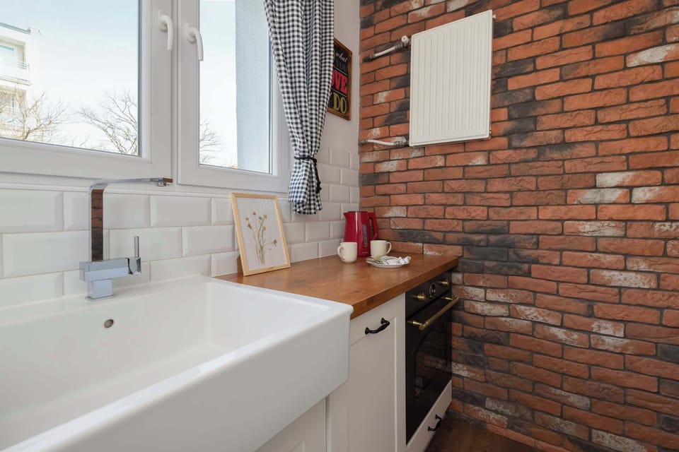 A rustic kitchen corner with an exposed brick wall, a farmhouse-style sink, and stylish wooden countertops under a wide window.