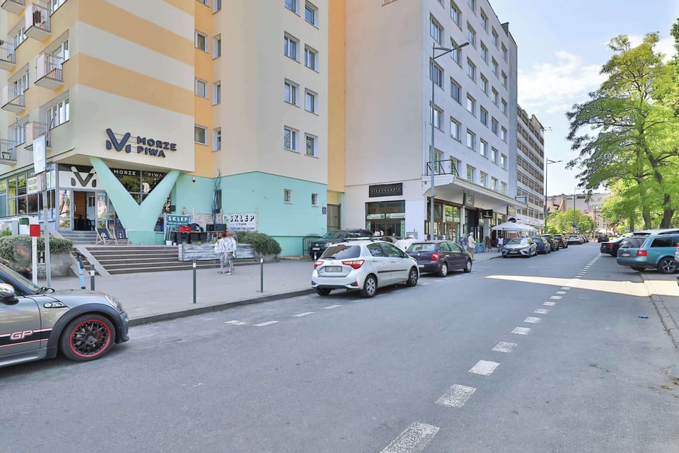 A street view with green trees, parked cars, and a bright blue sky.