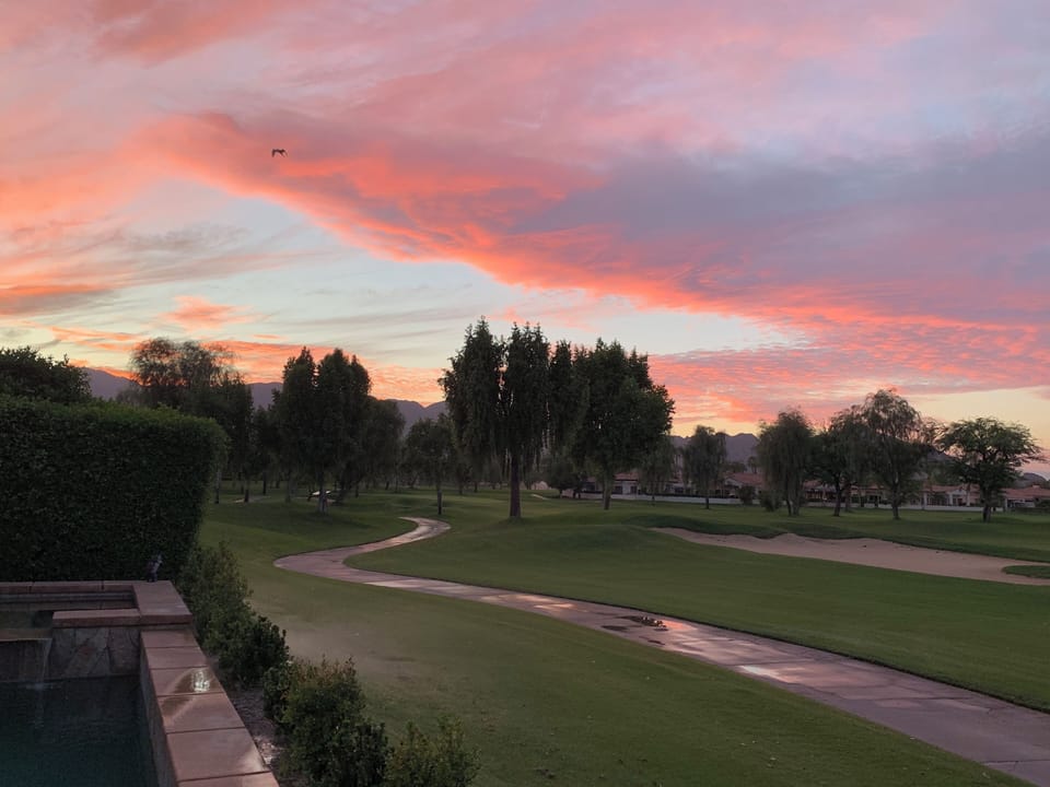 Desert golf course sunset with mountain views and pink skies.