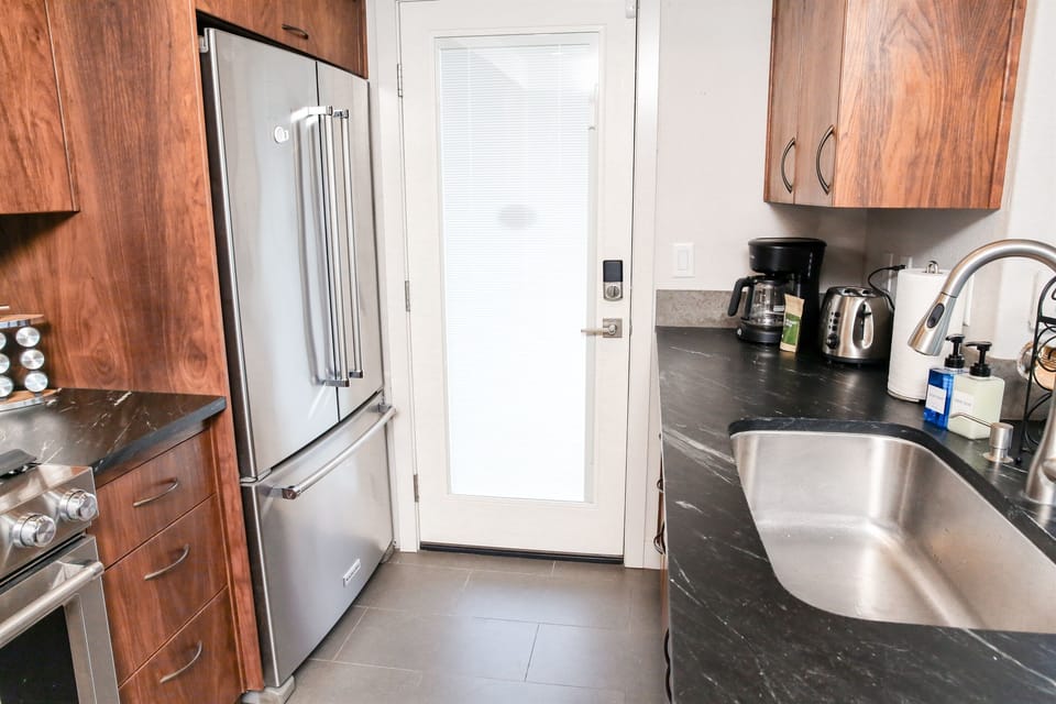 Showcasing the home's blend of warmth and modernity, this space features a suite of professional stainless steel appliances, including a French-door refrigerator, richly stained wood cabinetry, and sleek, dark stone countertops.