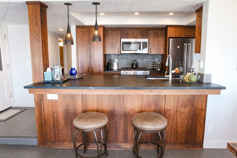 Entertain effortlessly in this gorgeous and spacious gourmet kitchen! Defined by its richly stained wood cabinetry and a massive, sleek dark stone island, this space offers ample preparation and bar seating.