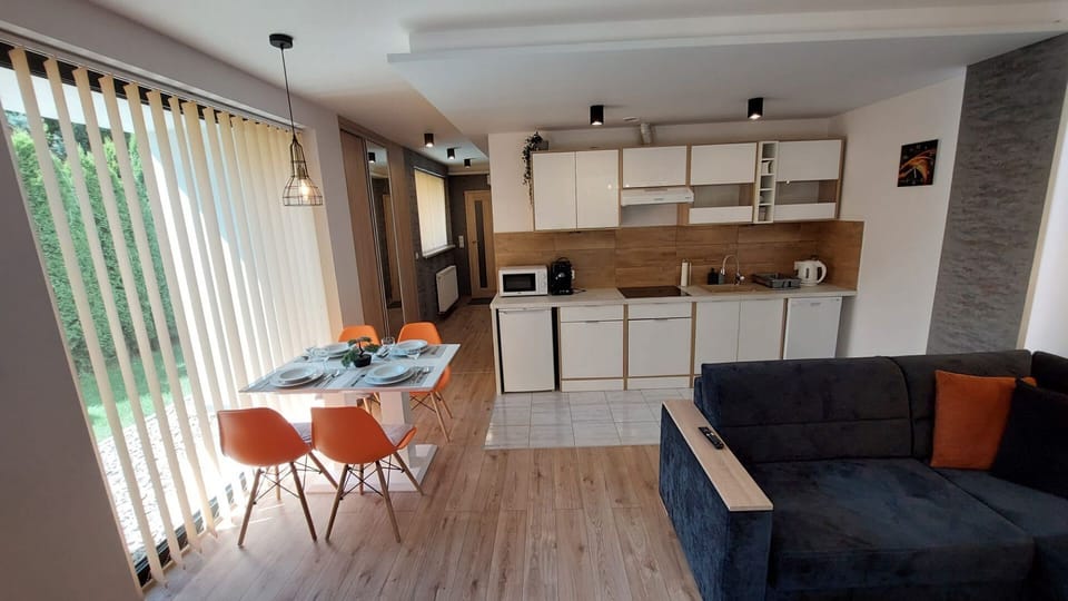 Open-plan kitchen and living room with orange dining chairs and large windows.