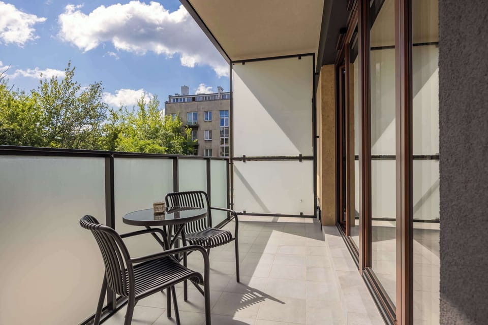 A furnished balcony with a small table and two chairs, overlooking a green area.