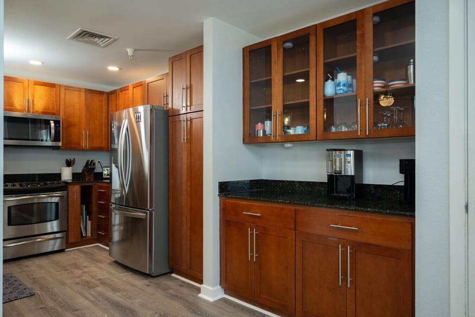 Fully equipped coastal kitchen with stainless steel appliances, rich wood cabinetry, granite countertops, and a built-in coffee station.
