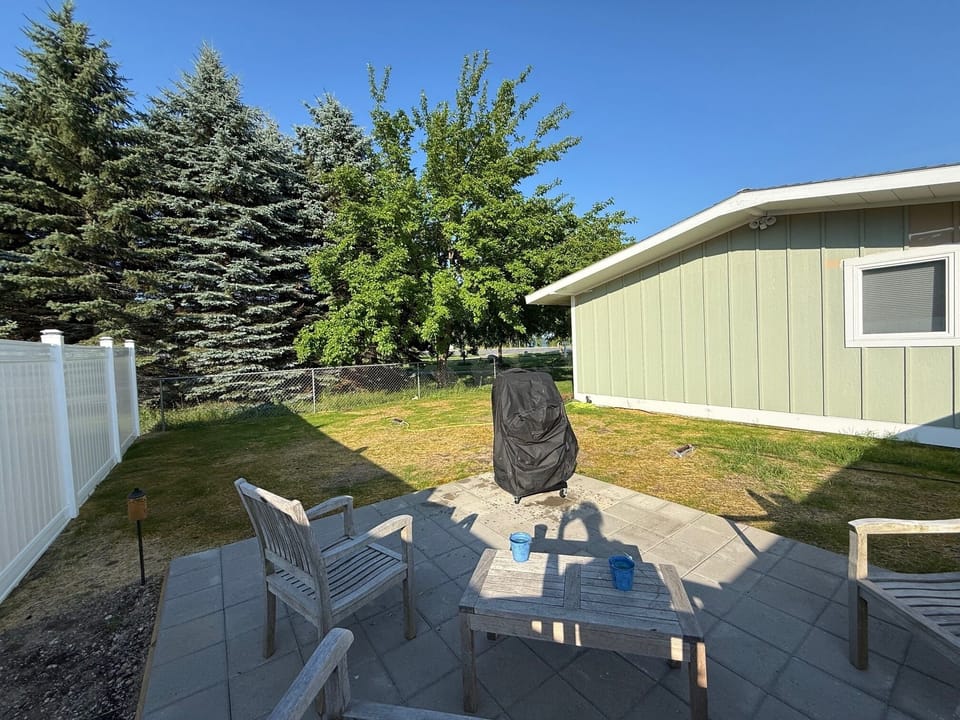Newly fenced backyard with raised patio with teak furniture and new grill.