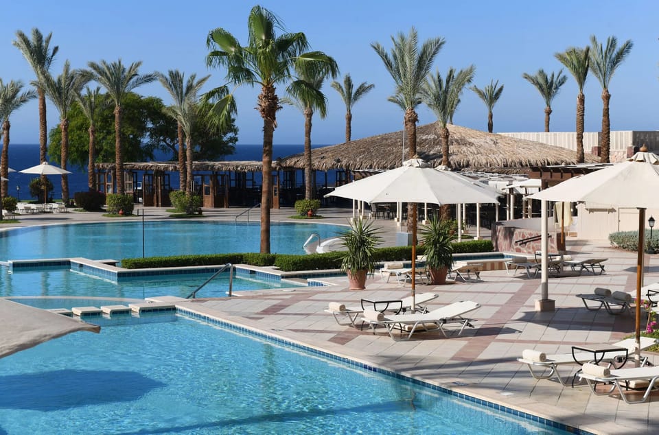 Lounge poolside with shaded cabanas and sparkling blue water.