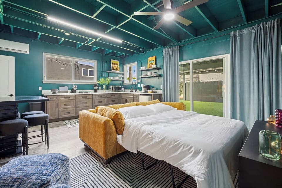 This versatile space boasts vibrant teal walls, a cozy bedroom with art, a modern kitchen, and a comfy sofa. Perfect for relaxing or entertaining!