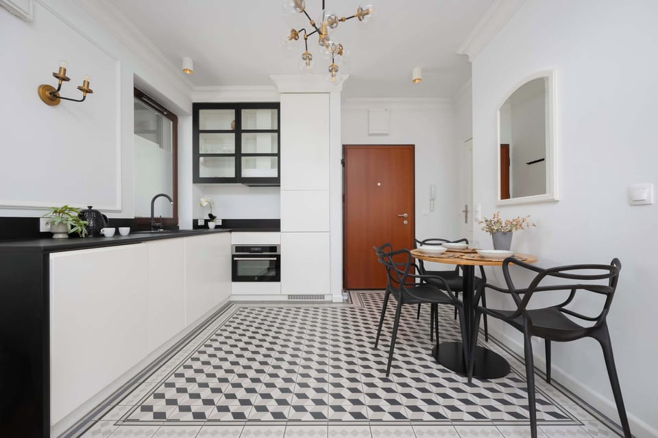A clean and modern kitchenette with white cabinetry, dark countertops, and a compact dining setup.

