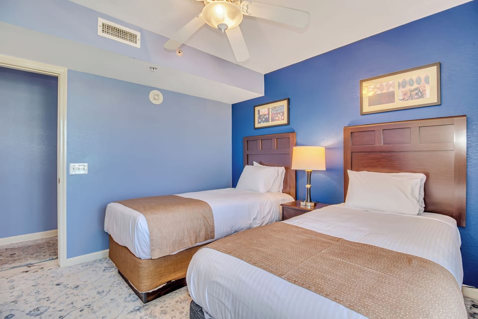 Unwind in your serene twin bedroom with crisp linens, calming blue walls, and gentle ceiling fan breeze creating the perfect retreat.