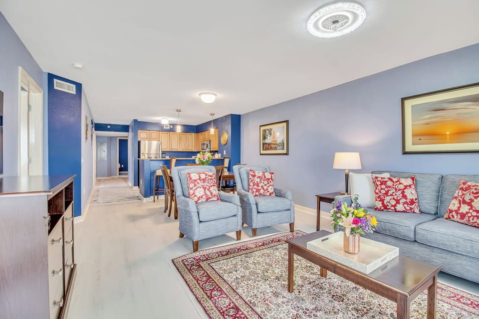 Relax in your spacious living room with plush seating, vibrant coral accents, and an open layout flowing into your fully-equipped kitchen.