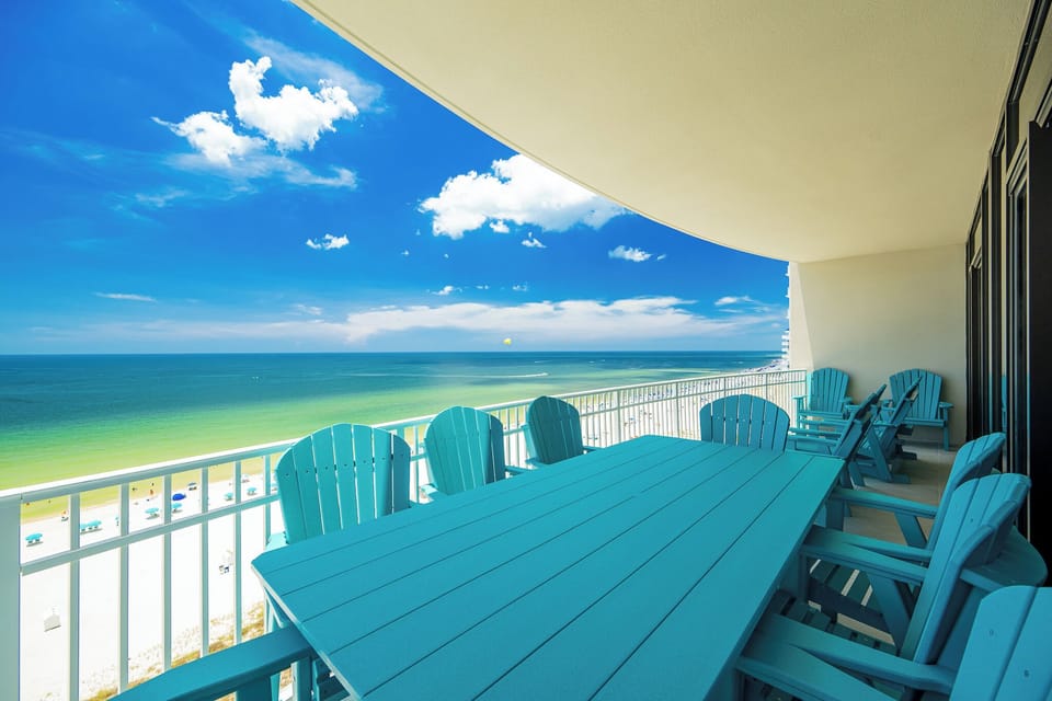 Relax at the spacious outdoor dining area, surrounded by vibrant blue chairs and a panoramic view of the beach