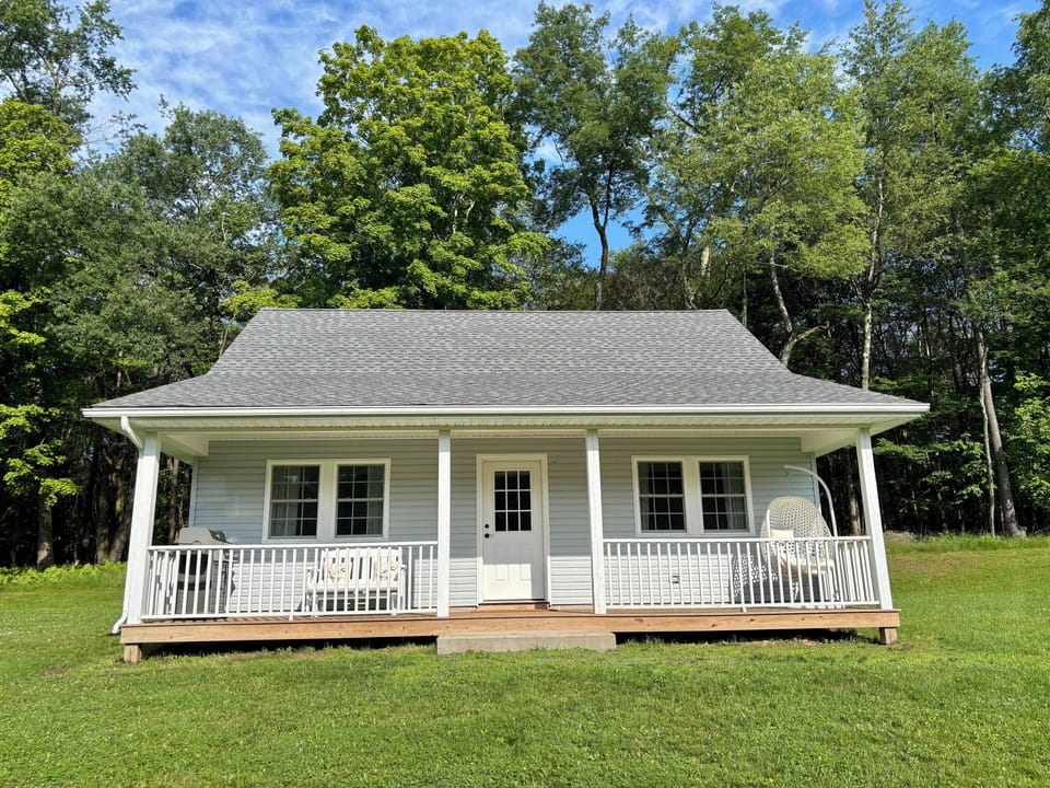 Cottage with a grill, porch swing, and seating.