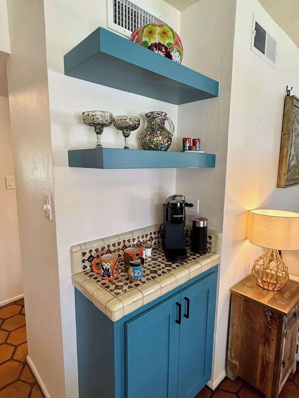 Charming built-in coffee station with vibrant Talavera mugs, a Keurig machine, and colorful floating shelves. The hand-painted Saltillo tile countertop adds warmth and Southwestern flair, making this cozy corner both functional and full of character.