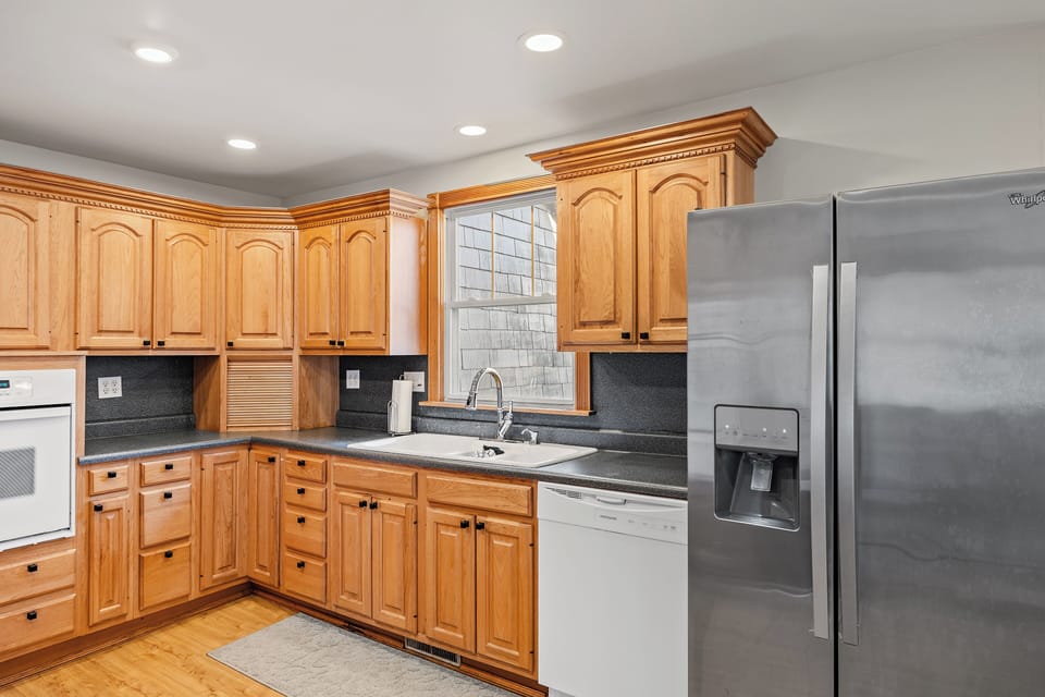 Modern kitchen with a refrigerator, dishwasher, and a sink by the window, perfect for cooking and enjoying natural light.