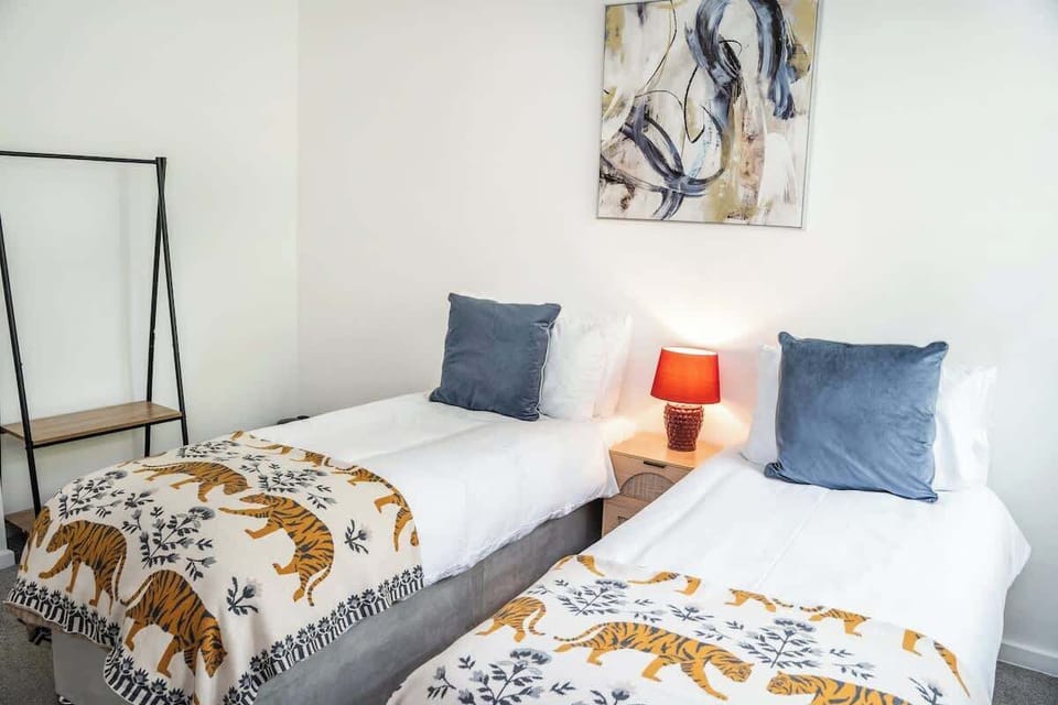 A bright, inviting twin bedroom. Blending crisp white linens with playful tiger-print throws, dusty blue pillows, and an eye-catching red bedside lamp, this space offers a charming, character-filled retreat.