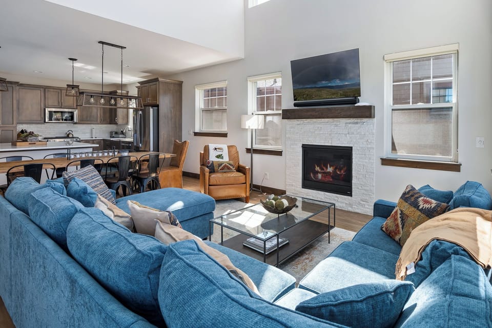 - Spacious open plan layout connects the cozy living room with the kitchen - Blue sectional and fireplace offer comfort for relaxing or socializing - Large windows, clean design, and rustic accents tie it all together