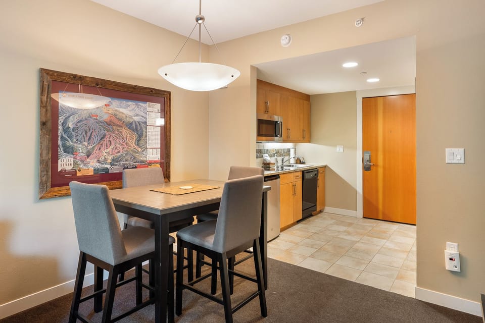 - Cozy four seat dining table framed by art and pendant lighting, ideal for shared meals - Fully stocked kitchen just steps away with stainless appliances and wood cabinets - Great layout for everything from snacks to full family dinners