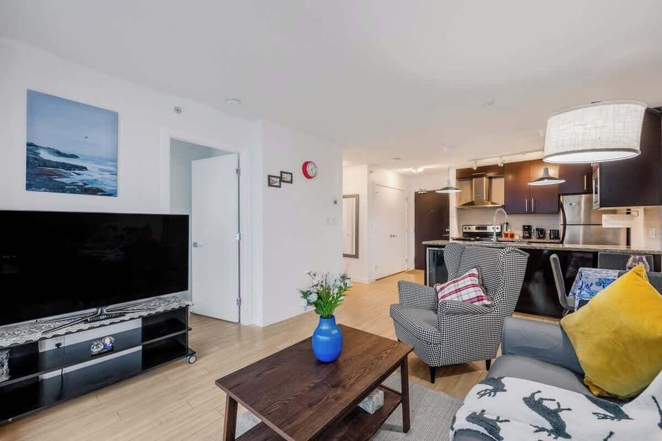 Panoramic view of the apartment's main living areas. Spacious living room flows into the full kitchen. Includes a large TV, comfortable seating, and bright accents. Enjoy the open concept, ideal for guests
