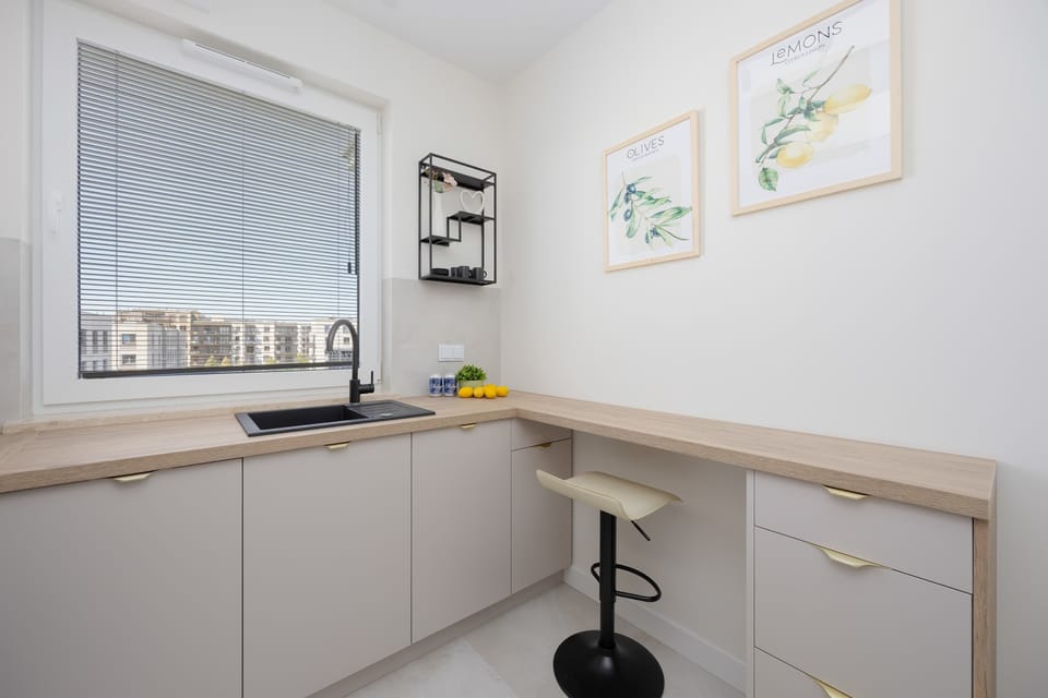 A clean kitchen corner with white walls, beige countertop, and a coffee machine by the window.