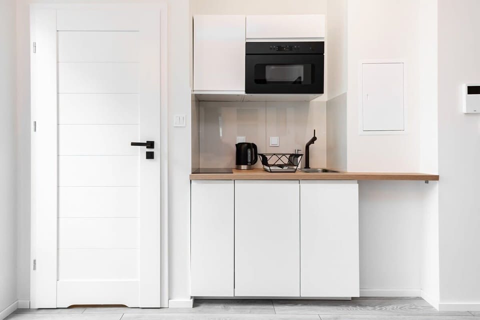 A well-organized kitchenette with a microwave, white cabinets, and a wooden countertop, maximizing functionality in a compact space.