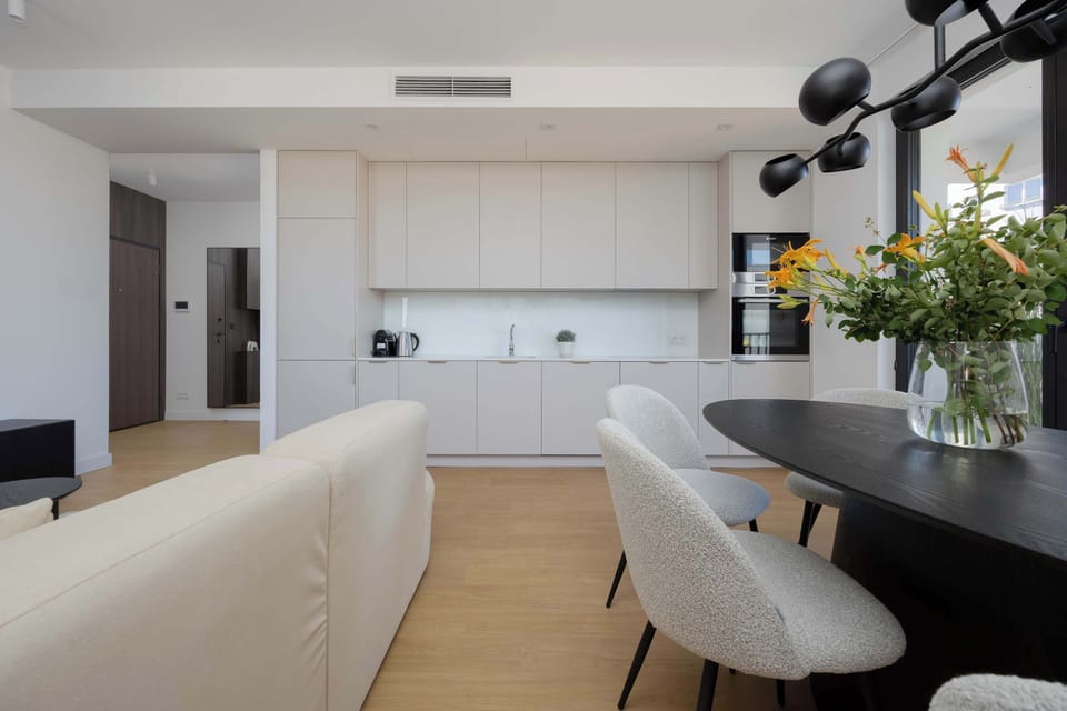 A contemporary kitchen and dining area with elegant black chairs, a round table, and white cabinetry.