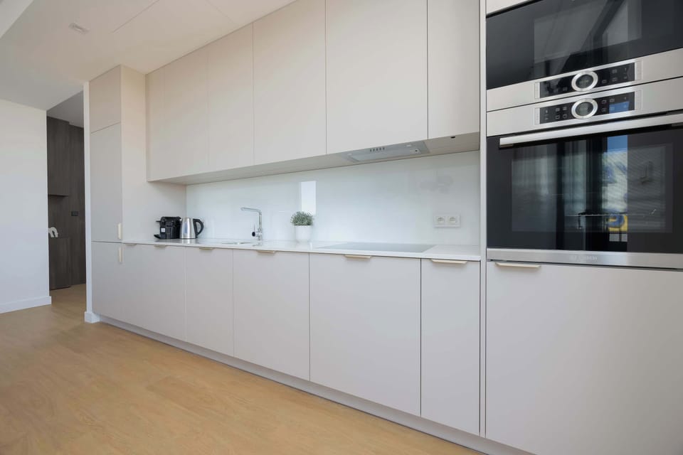 A long, sleek kitchen setup with matte white cabinets, built-in appliances, and a minimalist backsplash.