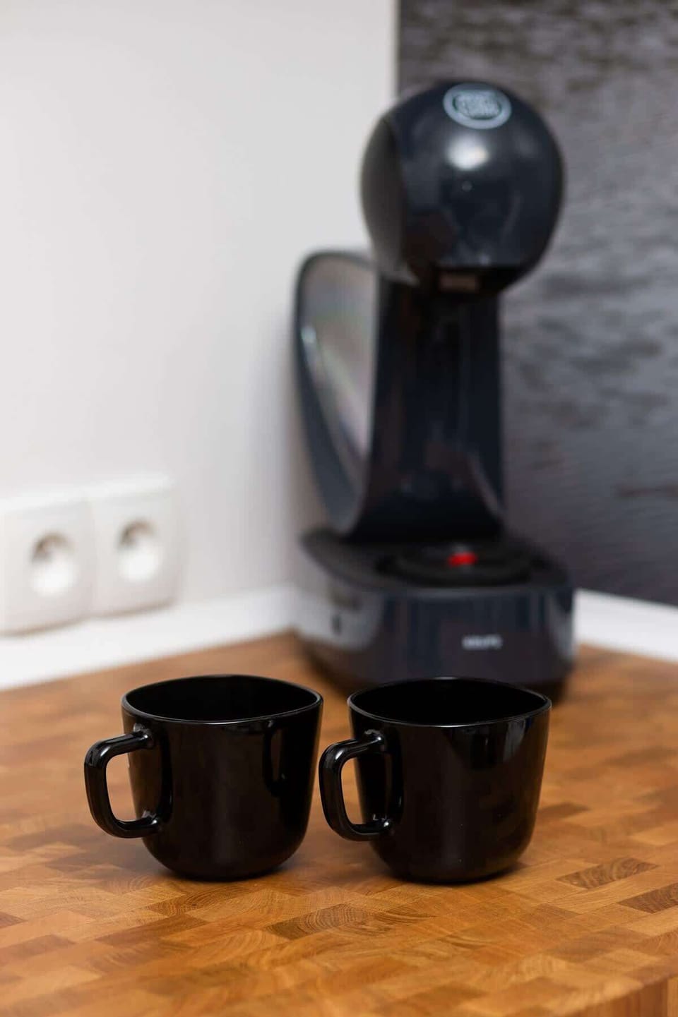A close-up of a decorative setup with two black coffee cups and a modern black figurine.