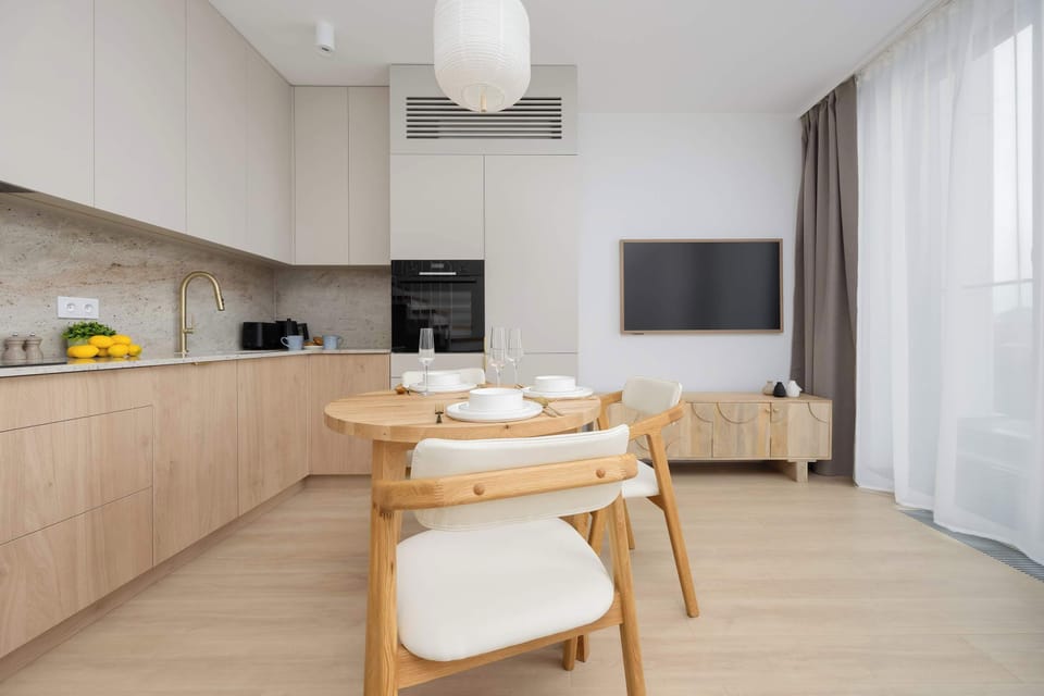 A kitchen with sleek cabinets and a dining area in warm, neutral tones. Soft lighting enhances the cozy and functional layout.