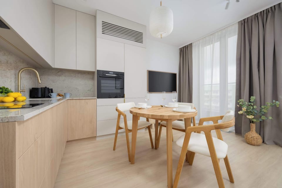 A modern kitchen with built-in appliances and a cozy dining table for four. The warm wooden finishes and subtle lighting create a welcoming space.

