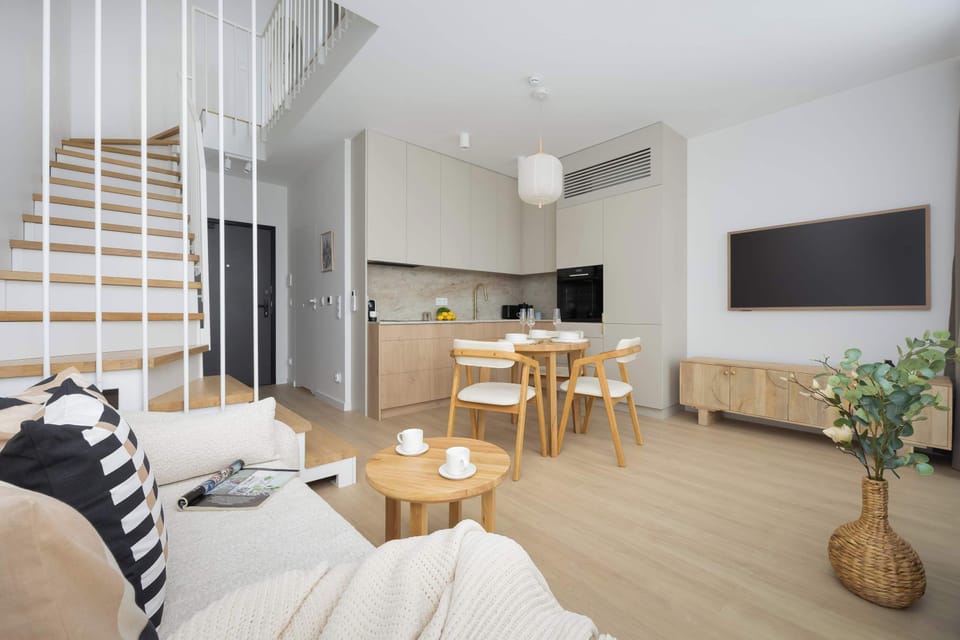 A living room area with a spiral staircase and comfortable seating. Natural light fills the space, highlighting the modern aesthetic.