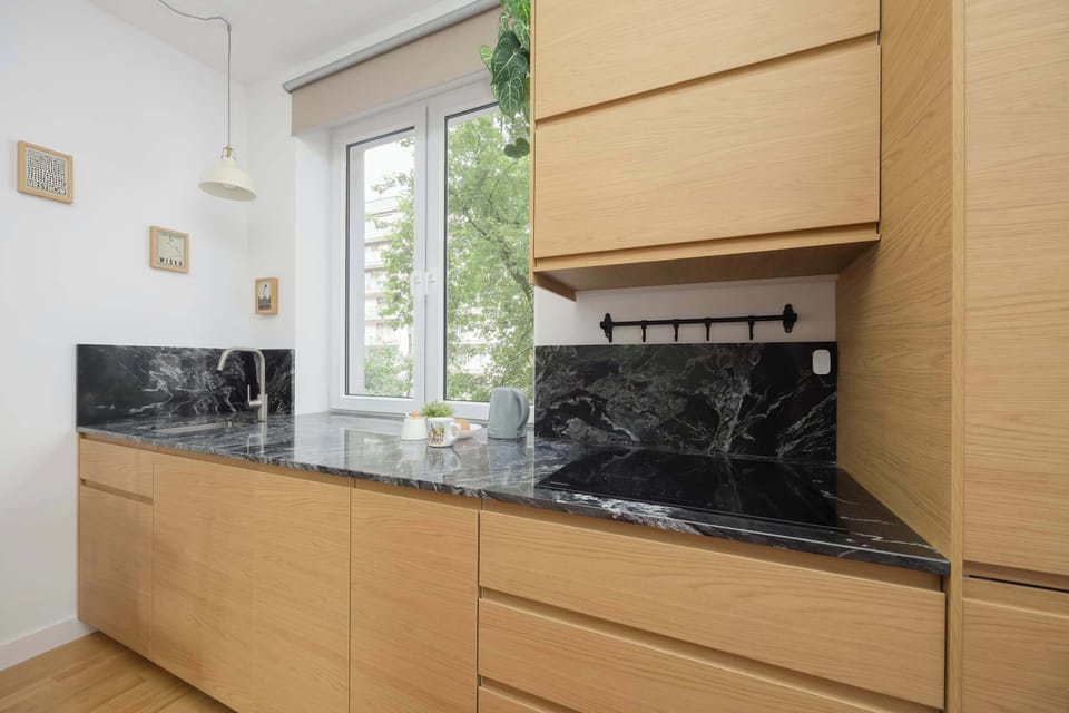 A close-up of the kitchen corner with a deep sink, light wooden drawers, and a marble countertop.
