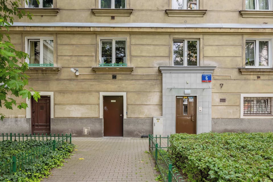 A classic tenement-style apartment building exterior with beige stone façade and small hedges.