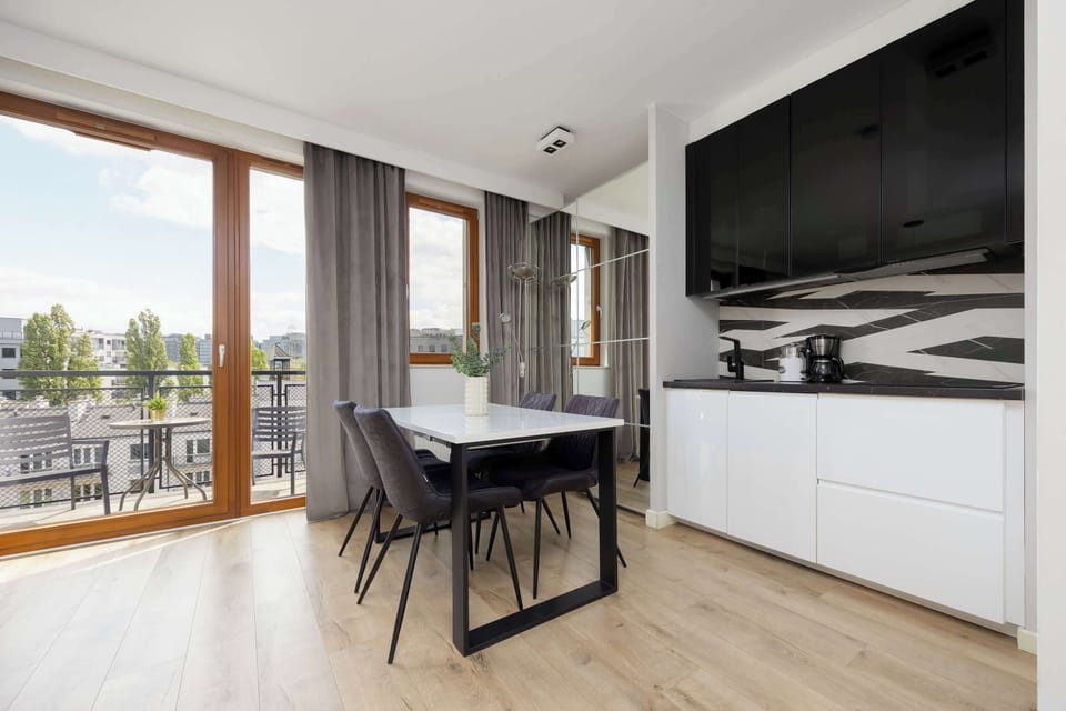 An open-plan living space with a dining table and chairs near floor-to-ceiling windows.