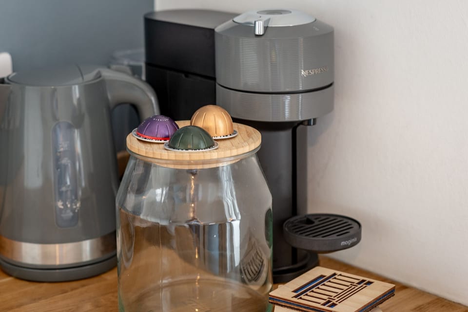 Coffee machine, kettle, and jar with colourful pods on wooden counter.