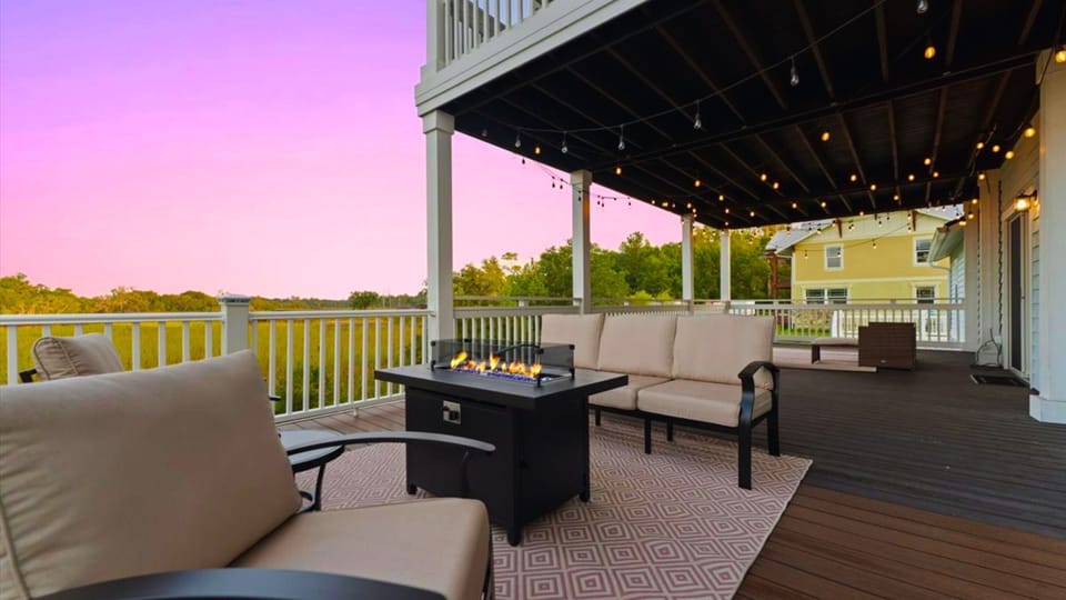 Sip wine by the fire table and take in serene marsh views from this dreamy covered deck. With cozy cushioned seating, string lights overhead, and the soft glow of sunset, this outdoor space is