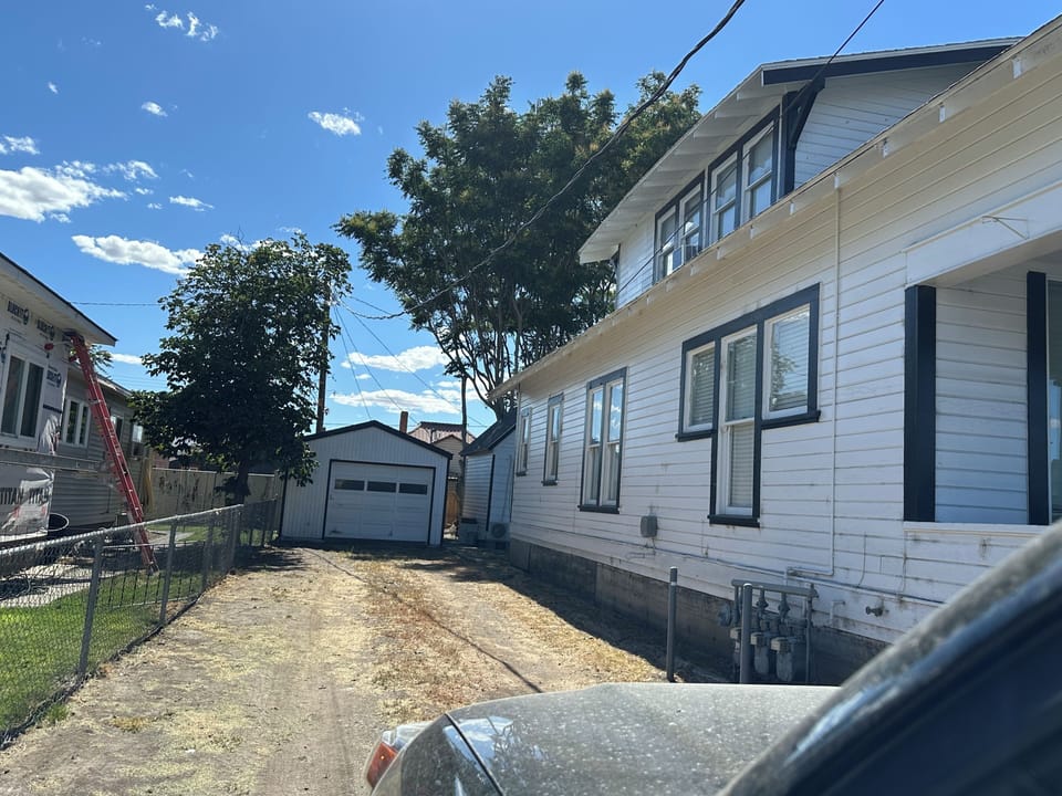 House is located behind the large house next to the garage in this photo. 