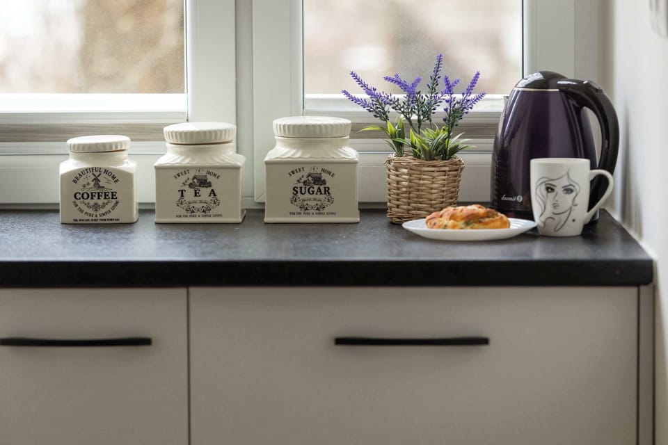 A close-up of a kitchen countertop displaying decorative mugs, a kettle, and a small plant, adding a cozy touch.